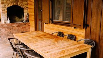 Un'area pranzo all'aperto con tavolo in legno, sedie in metallo, un camino in pietra e pannelli di legno alle pareti.
