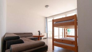 A living room with a sofa, a round table with a vase and glasses, and a wooden bunk bed.