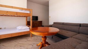 A room with a bunk bed, a sofa, a wooden table, and a television on a cabinet.