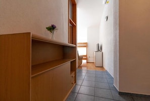 Ein schmaler Korridor mit einem Holzschrank, einem kleinen Tisch mit einer Vase und einem Kühlschrank.