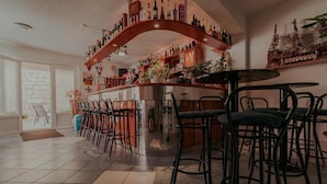 Eine Bar mit einer geschwungenen Holzkonstruktion, mehreren Barhocker und einer Auswahl an Flaschen in Regalen.