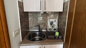 A compact kitchen with two cabinets, a sink, and a small countertop with a dish rack.
