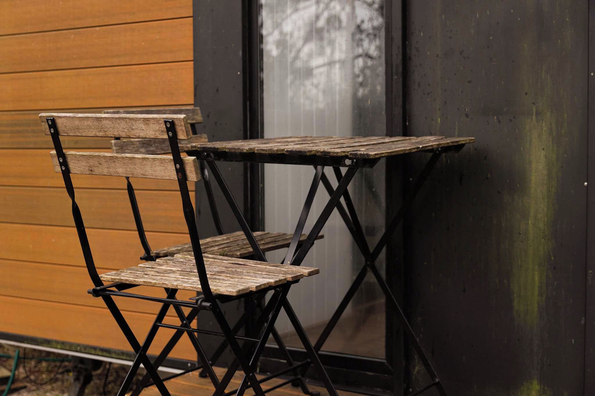 Une table et une chaise pliantes, adossées à un mur en bois près d’une fenêtre.