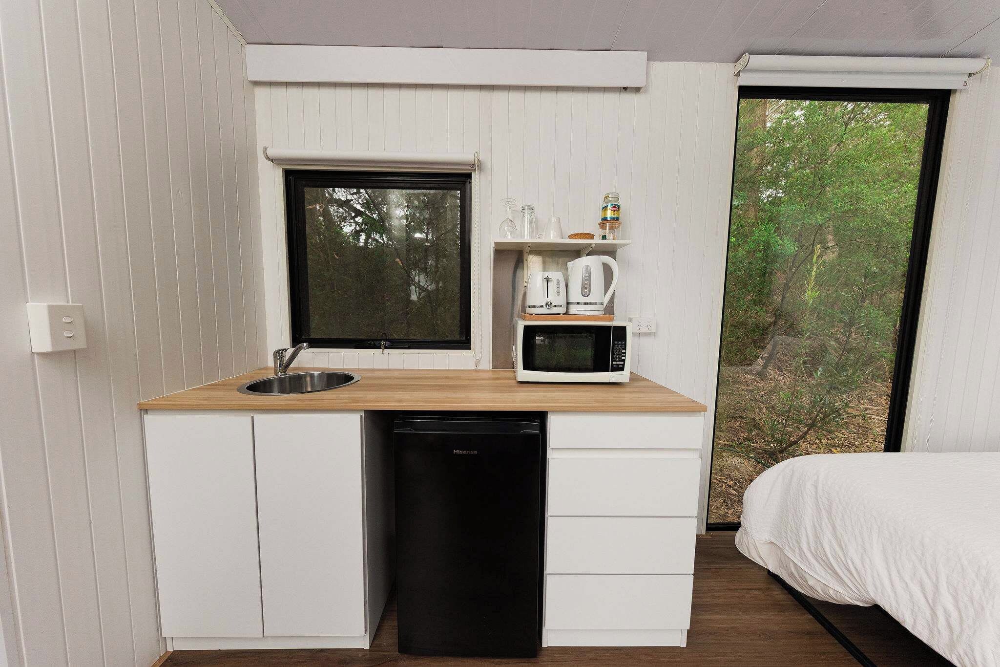 Una kitchenette funcional con pileta, microondas y estantes de almacenamiento.