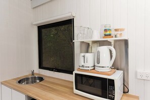 Cocina compacta con microondas, cafetera y repisa con cristalería y un frasco.