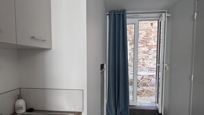 En smal hall med ett köksområde på vänster sida, en dörr som leder ut till en uteplats och en dörrmatta med texten "Chic Jungle".