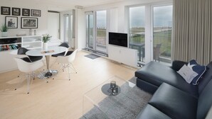 Ein modernes Wohnzimmer mit grauem Sofa, einem Esstisch mit Stühlen und einem Fernseher auf einem Balkon.