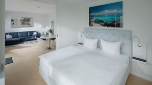 Ein modernes Hotelzimmer mit einem großen Bett, einem Schreibtisch, einer Couch und einem Bild mit Strandmotiv.