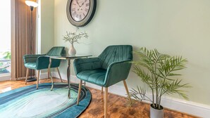 Ein Zimmer mit zwei Türkis-Stühlen, einem runden Tisch, einer Uhr, einer Pflanzvase und einem Holzboden.