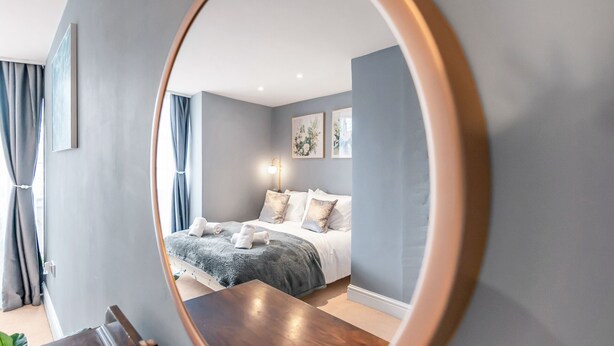 Ein Schlafzimmer mit einem Bett, einem Nachttisch, einem Spiegel und einem Fenster mit Vorhängen.