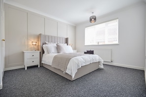 Quarto com cama, mesas de cabeceira, janela com persianas e luminária no teto.