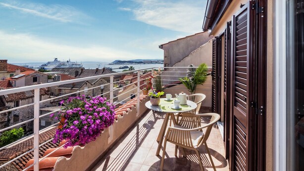 A balcony with a table and chairs, potted plants, and a view of the sea and distant ships. - Lucio suites - Apartment 3 with balcony (Split)