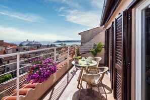 Un balcon avec une table et des chaises, des plantes en pot et une vue sur la mer et les navires au loin.