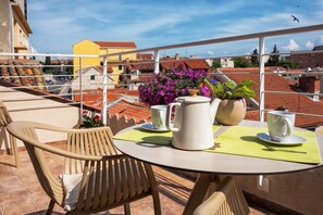 A balcony with a table set for two, featuring a white pitcher, two white cups, and a vase with purple flowers.