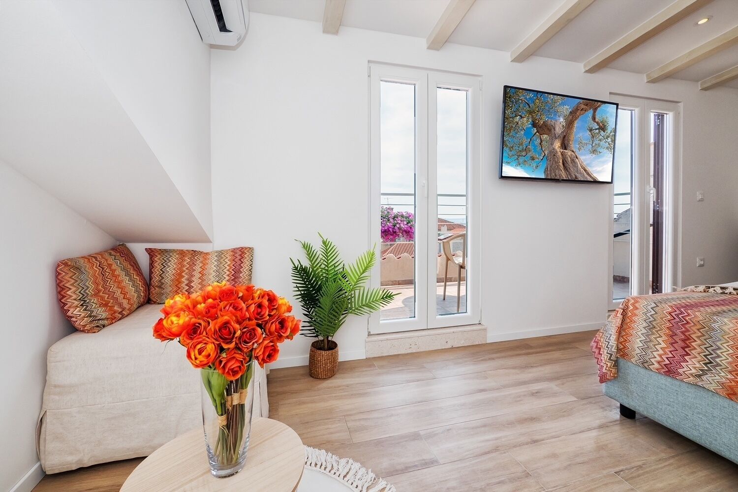 A modern living room with a sofa, a coffee table with a vase of flowers, and a large window with a view of the outdoors.