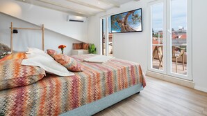 A bedroom with a bed, pillows, a nightstand, a TV, and a large window with a city view. - Lucio suites - Apartment 3 with balcony (Split)