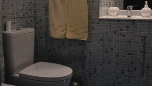 Ett badrum med toalett, bidé och handfat. Två handdukar hänger på väggen.