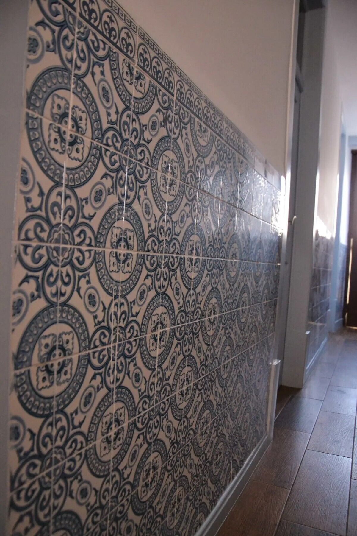 A hallway with patterned tiles on the walls and a wooden floor.
