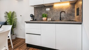 A modern kitchen with white cabinets, a built-in microwave, a sink, and a countertop. There is a potted plant and a small table with chairs.