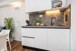 Une cuisine moderne avec des armoires blanches, un four à micro-ondes encastré, un évier et un plan de travail. On y trouve une plante en pot et une petite table avec des chaises.