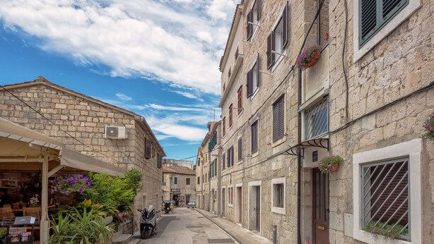 A narrow street with stone buildings, a shop on the left, and a parked car in the distance.