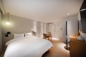 A hotel room with a large bed, a desk, a chair, and a desk lamp.