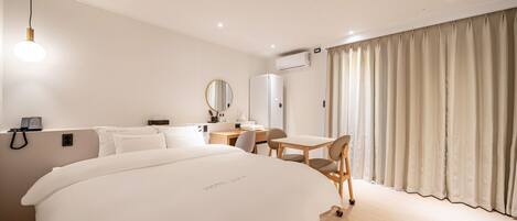 Quarto de hotel com uma cama grande, uma escrivaninha com cadeira, um espelho e uma janela com cortinas.