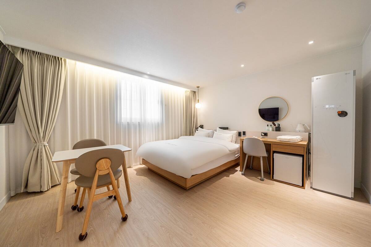 A modern hotel room with a bed, desk, chair, and a small refrigerator.