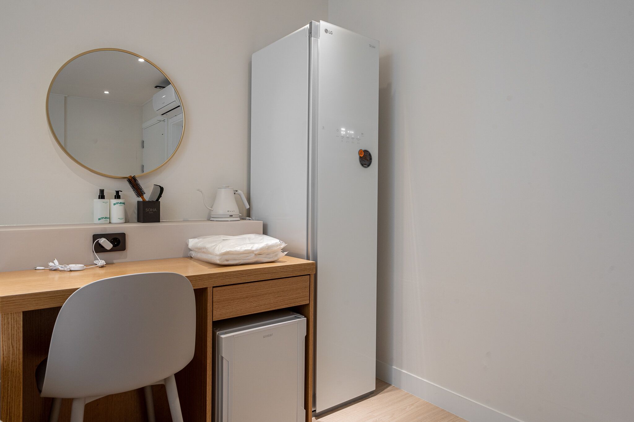 Habitación pequeña con escritorio de madera, un refrigerador compacto, espejo y lavamanos.
