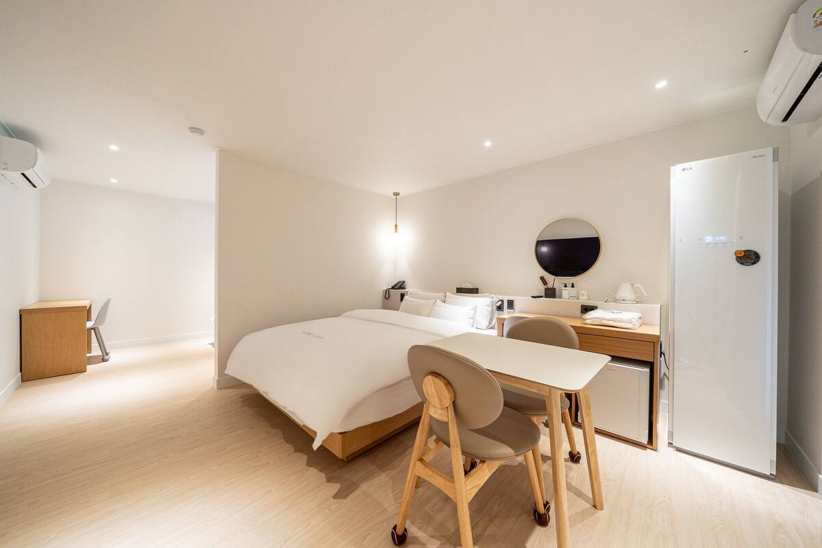 A modern hotel room with a bed, desk, chair, and a small kitchenette.