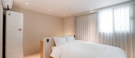 Ein modernes Hotelzimmer mit einem großen Bett, einer fest installierten Heizung und einem Fenster mit durchsichtigen Vorhängen.