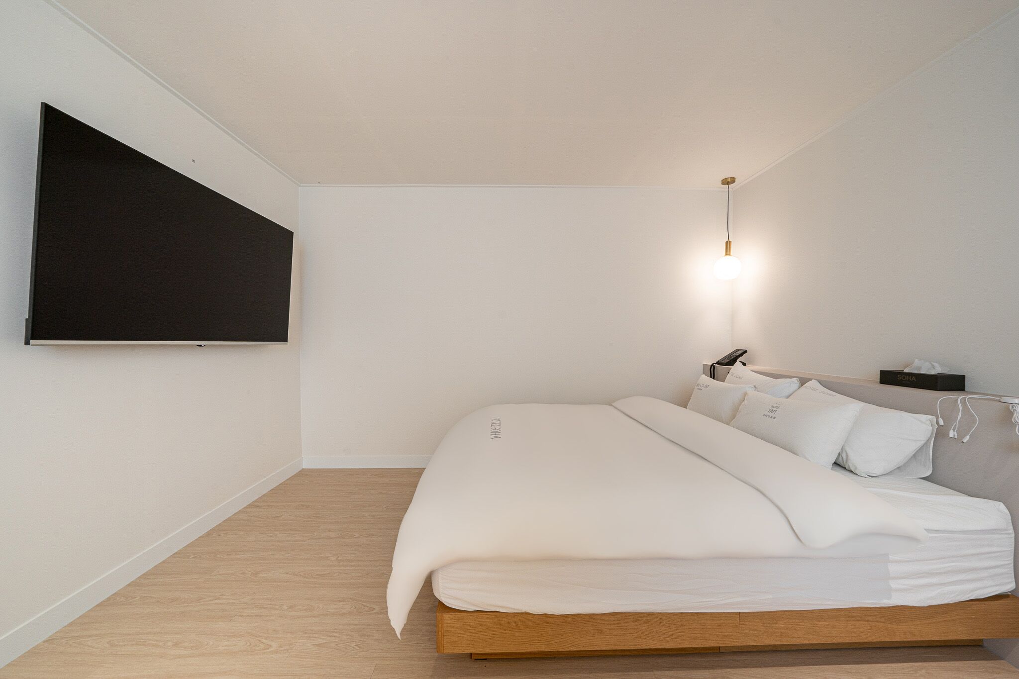 Une chambre à coucher au style minimaliste, avec un lit, un téléviseur fixé au mur et une table de chevet avec une lampe.