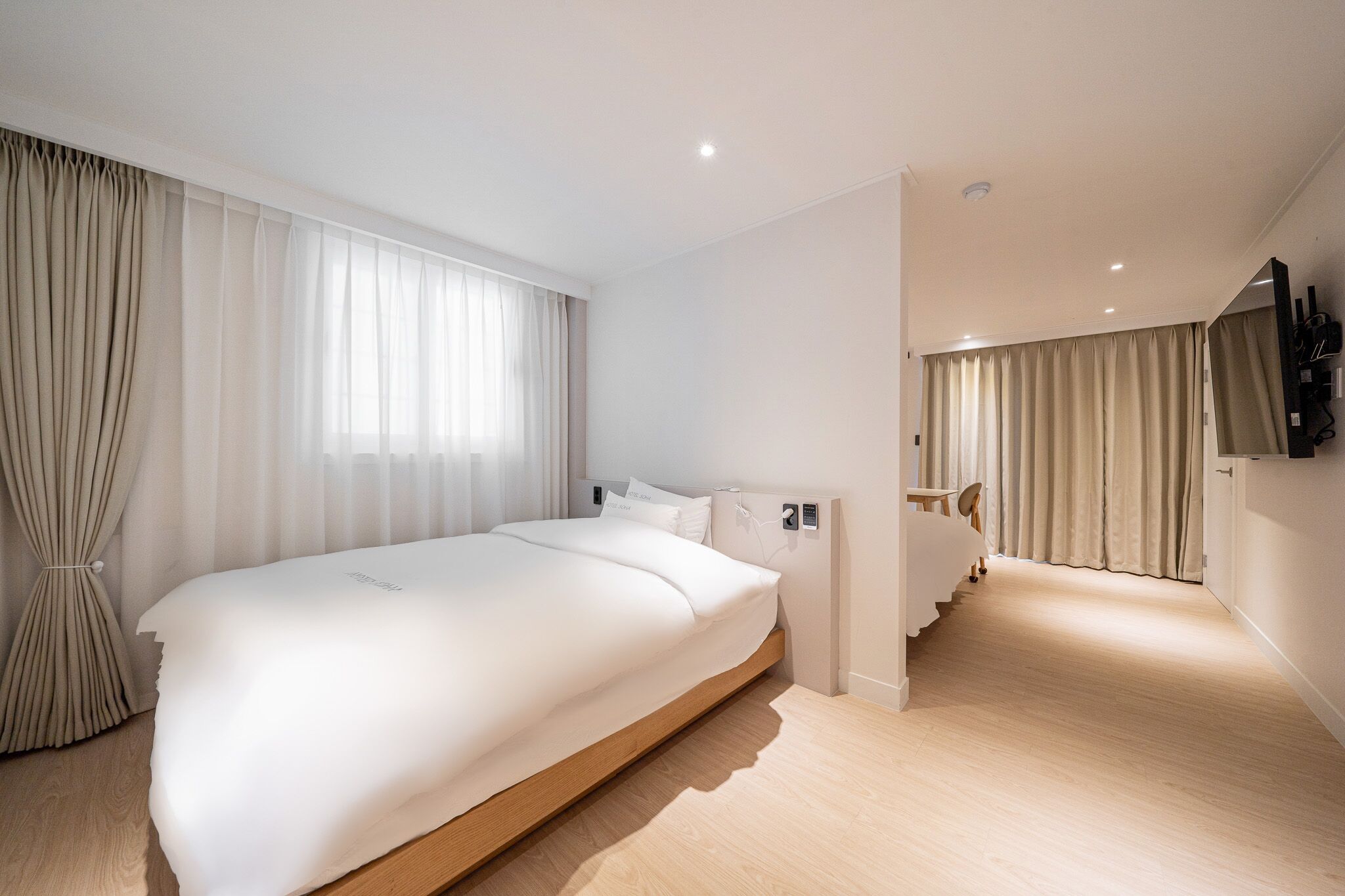 A modern hotel room with a large bed, a desk, and a television mounted on the wall.