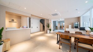 Un hall d’accueil moderne avec un comptoir en bois, un espace salon avec une table et des chaises en bois, et un escalier menant aux autres parties de l’hôtel.