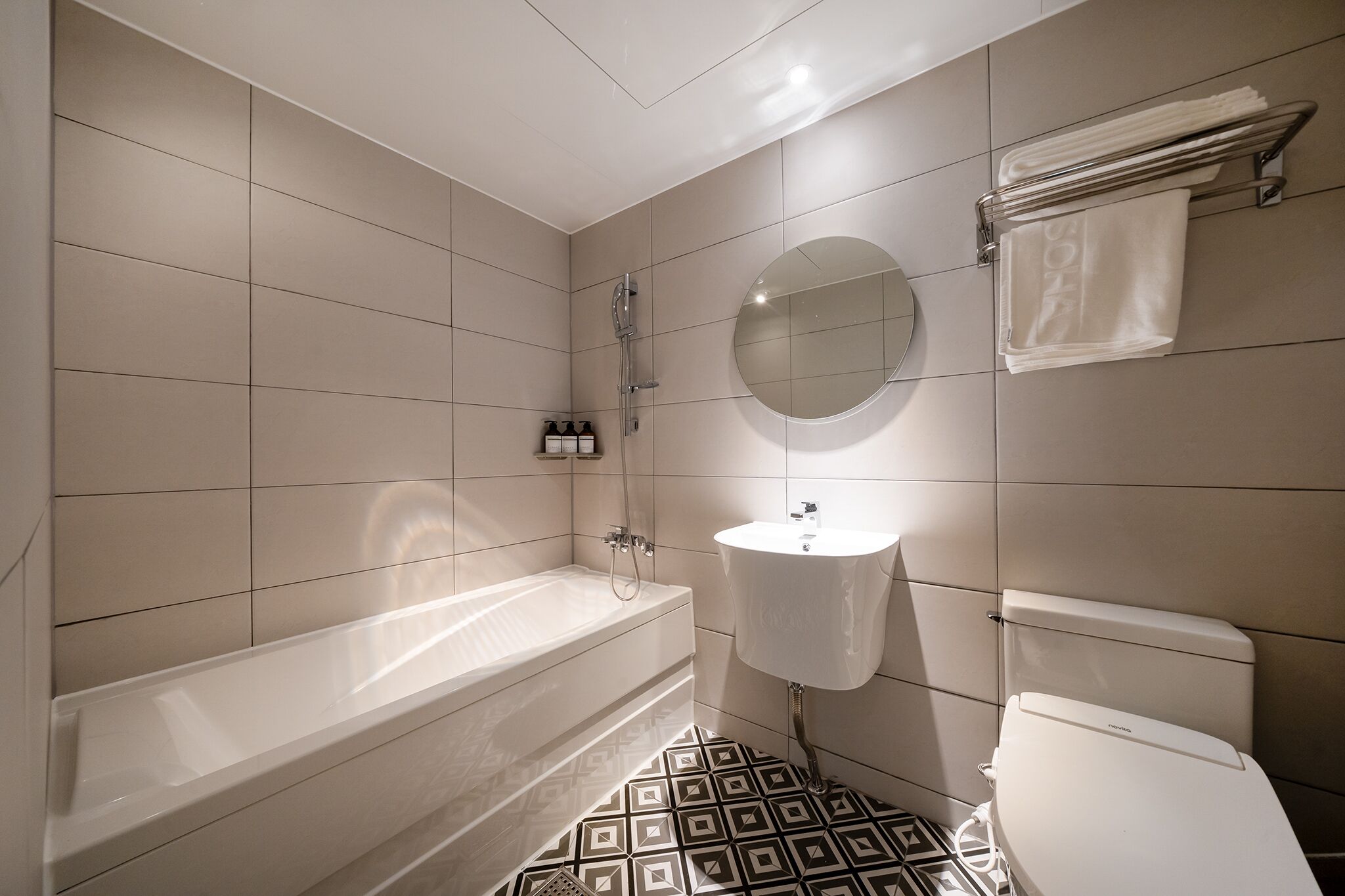 Un baño moderno con bañera, lavamanos e inodoro, que destaca por un suelo con estampado geométrico.