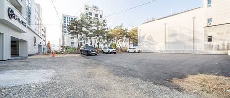 Un hotel con fachada moderna, un estacionamiento con varios coches y suelo de grava.