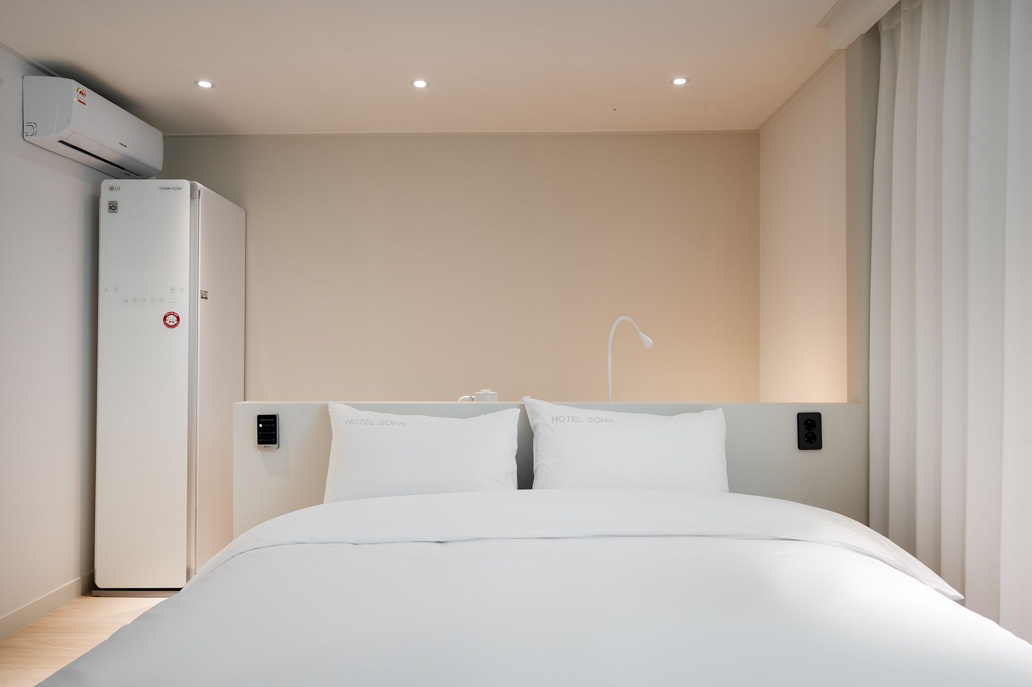 A modern hotel room with a bed, a wall-mounted air conditioner, and a control panel.