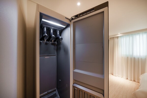 Habitación compacta y moderna con minibar integrado, ventana grande con cortinas translúcidas y cama con ropa blanca.