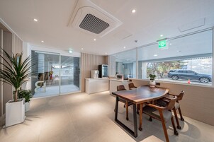 A modern hotel lobby with a wooden conference table, seating, a reception desk, and a large window with a view of the street.