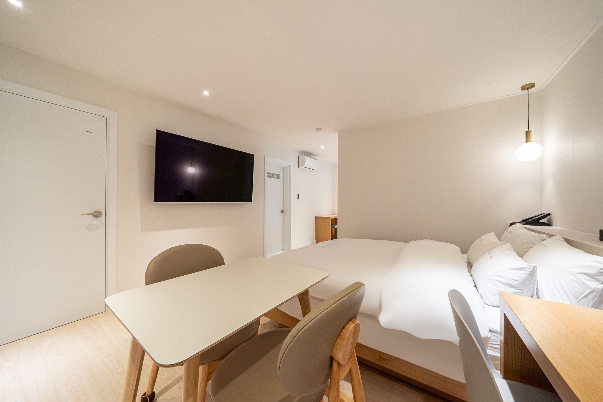 Et hotelværelse med en seng, et skrivebord, en stol, et fjernsyn ophængt på væggen og et natbord.