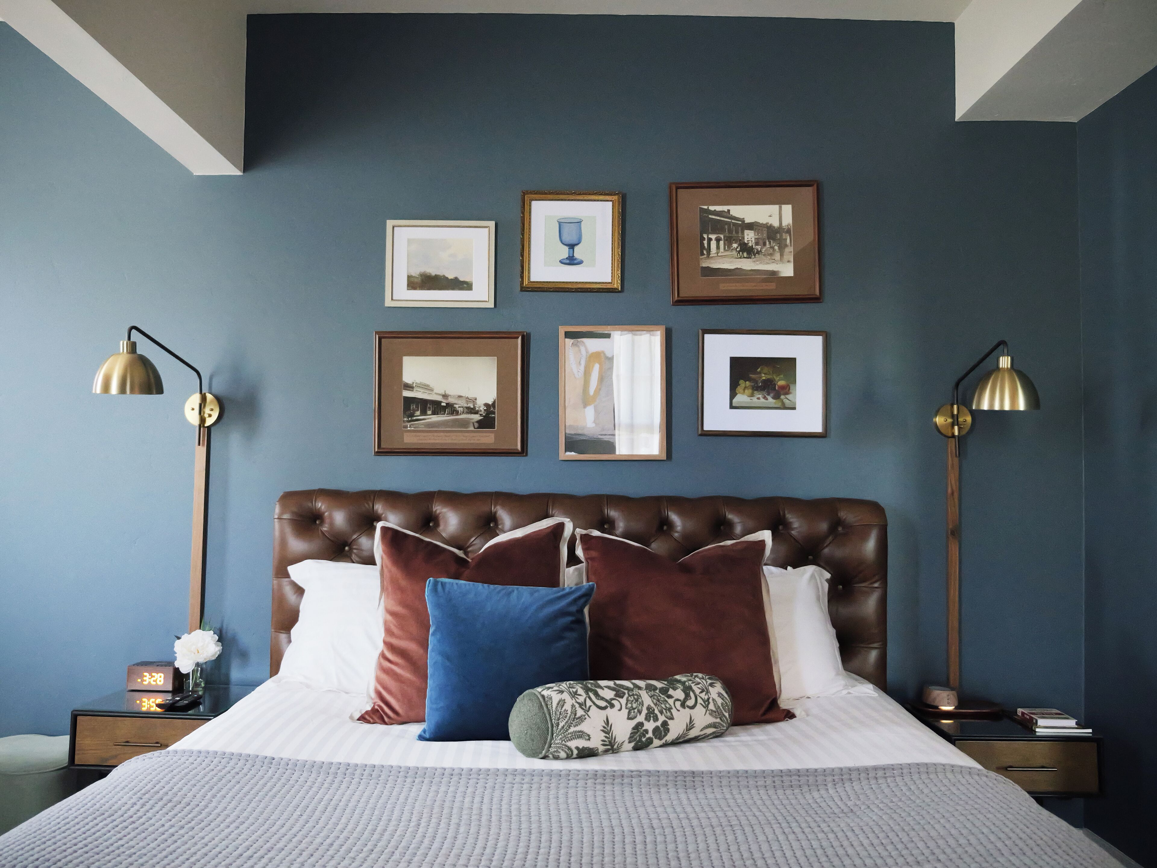 Ein Schlafzimmer mit einem großen Bett, vielen Kissen, einem Nachttisch und gerahmten Bildern an der Wand.