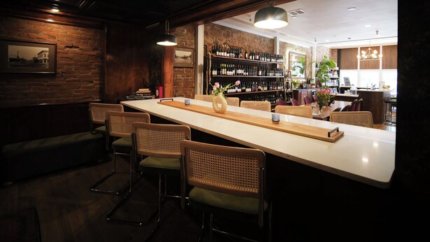 A bar area with a long counter, wicker chairs, and a wine rack in the background.