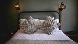 A bed with a metal headboard, two decorative pillows, a quilted blanket, and two wall-mounted lamps.