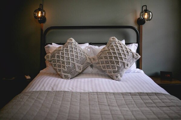 A bed with a metal headboard, two decorative pillows, a quilted blanket, and two wall-mounted lamps.