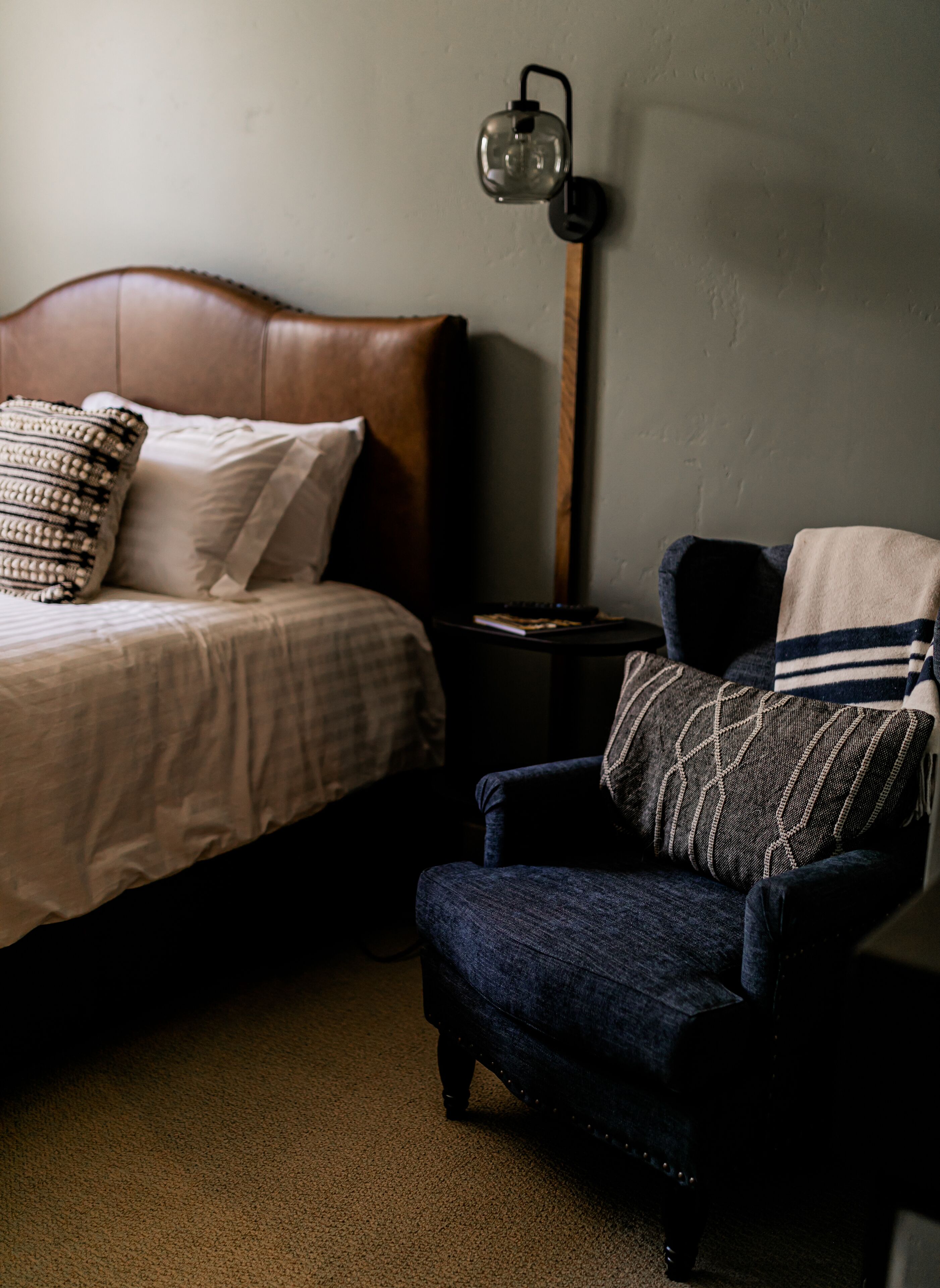A bedroom with a bed, a chair, a lamp, and a nightstand.