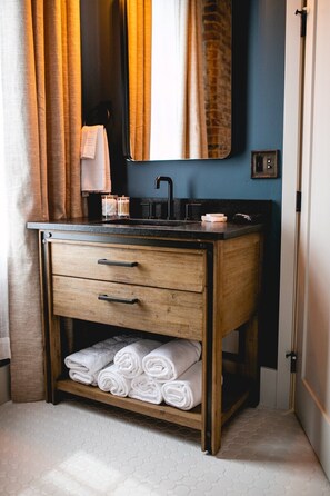 A bathroom with a wooden vanity, a sink, and a shelf with rolled towels. - Experience charming Jacksonville, OR in this 8-bedroom Historic Inn. Enjoy a wine country getaway with 8 private bedrooms. Walk to dining, shopping, and the famed Britt Festival grounds. (Jacksonville)