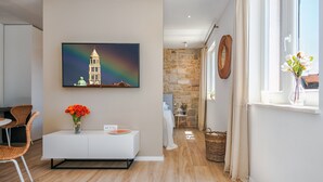 A modern living room with a large painting of a tower, a white console table with a vase of flowers, and a stone wall in the background. - Lucio Suites- Apartment 2 (Split)