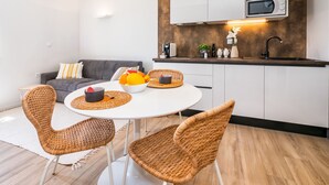 A modern kitchen with white cabinets, a microwave, and a sink. There is a dining area with wicker chairs and a white table. - Lucio Suites- Apartment 2 (Split)
