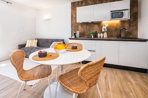 A modern kitchen with white cabinets, a microwave, and a sink. There is a dining area with wicker chairs and a white table.