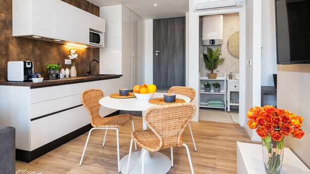 A modern kitchen with white cabinets, a microwave, and a dining area with wicker chairs and a white table. - Lucio Suites- Apartment 2 (Split)